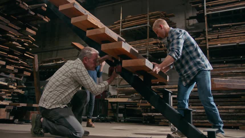 Men placing wooden sheets on a metal ladder inside a factory