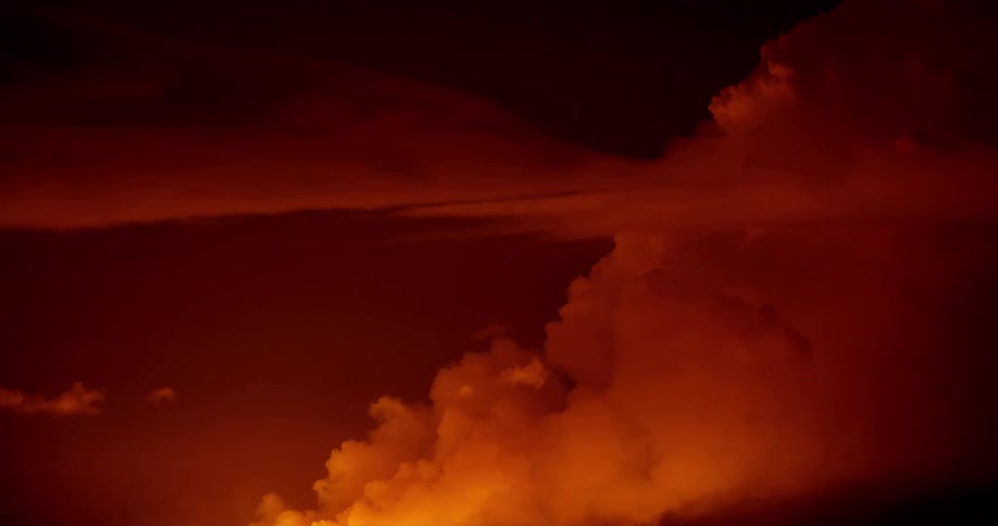Thick yellow and orange toned clouds of smoke slowly rising in a deep orange and red sky