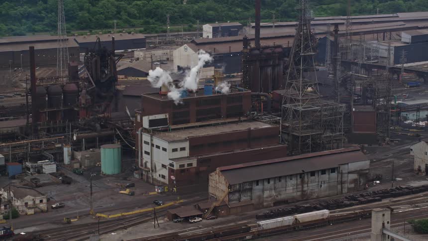Aerial panorama of a metallurgical plant with chimneys releasing smoke on the edge of a river canal