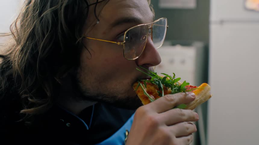 Man taking a slice of pizza and eating it while having a concentrated facial expression