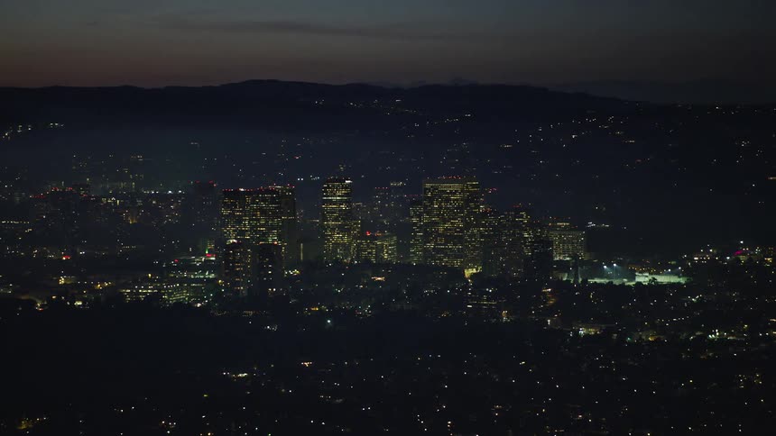 Lights glow from a metropolis with mountains in the dark behind it