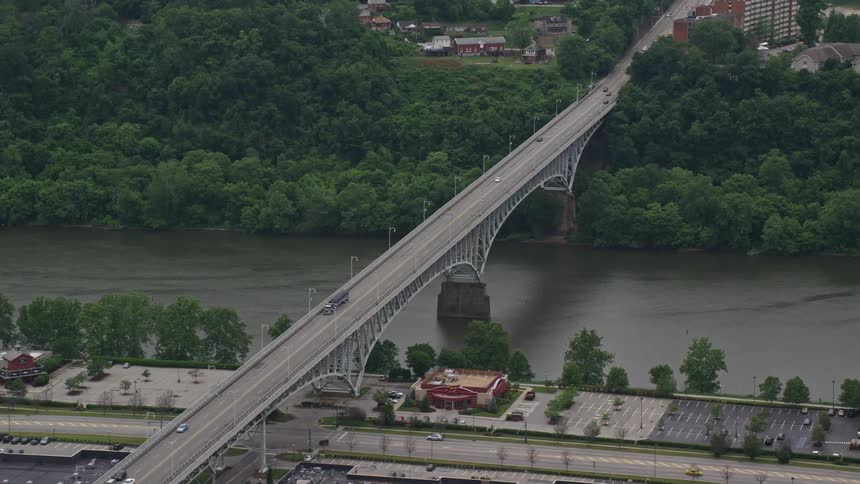 Vehicles travel over a bridge that spans a river thats lined with trees