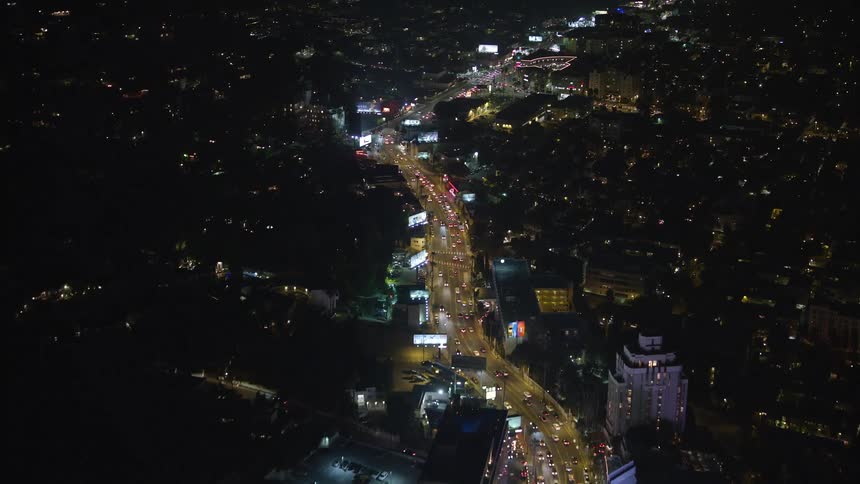Aerial view over lights illuminating the main strip through a metropolitan area surrounded by dark neighborhoods with small scattered lights