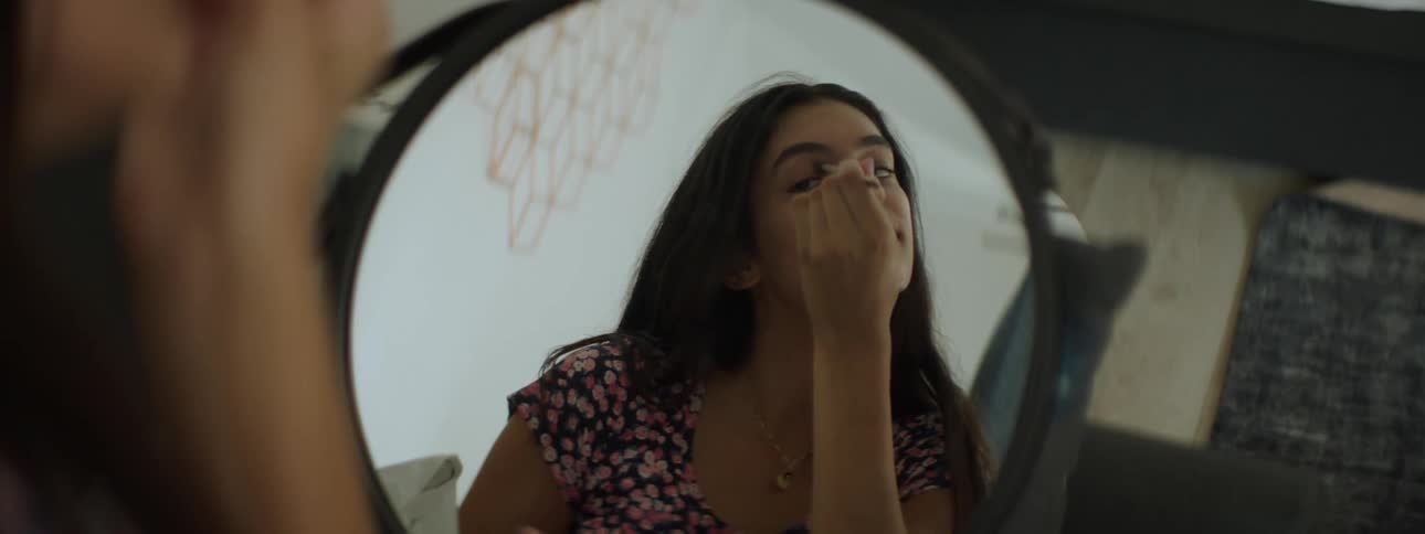 Young smiling woman putting makeup on her eyes while looking in a mirror