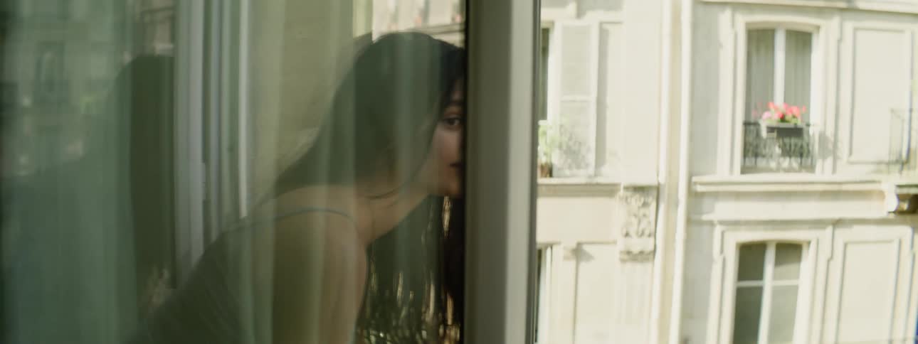 A woman drinks from a mug while looking out the window