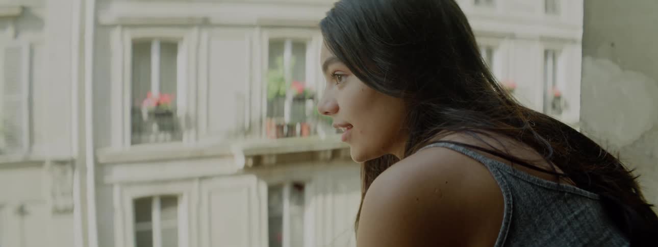 Young woman drinks a hot beverage while looking at the city from a balcony