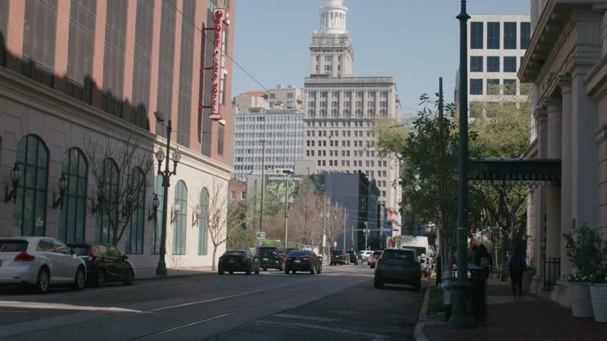Street with parked vehicles and pedestrians in a metropolis with commercial buildings on a cloudless blue sky day