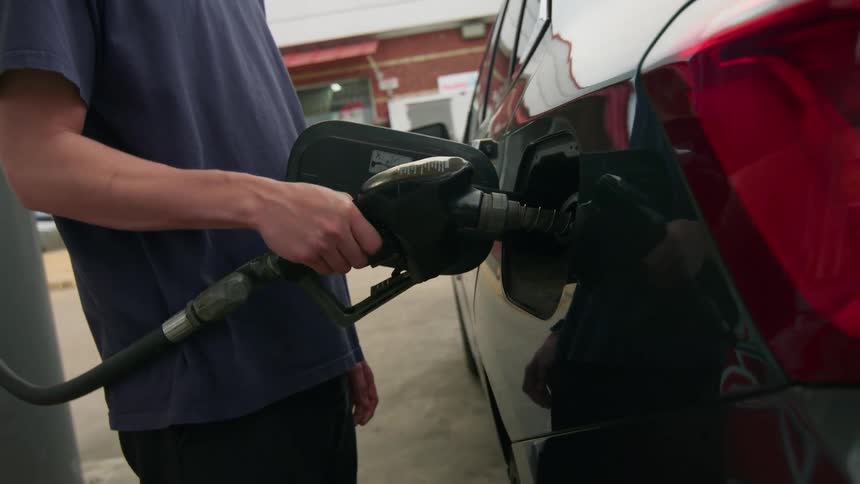 A person refueling a car at a gas station with the fuel nozzle inserted into the cars tank