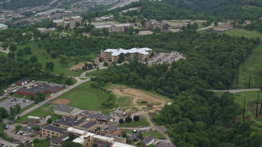 Aerial view of a campus with buildings and parking lots among trees and a large central field