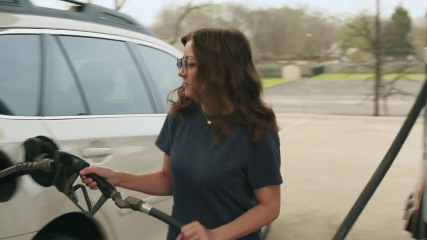 Woman is at a gas station in a suburban area filling up her car