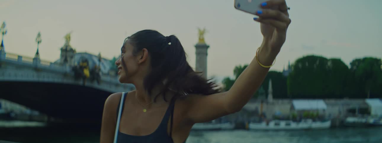 A young woman filming herself with a smart phone in front of a bridge in Paris, France