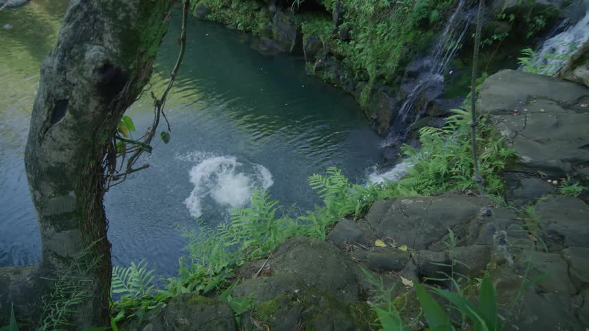 Man hanging from a rope and throwing himself off a cliff towards a river with a waterfall