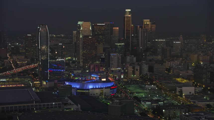 Aerial panorama of a metropolis with modern buildings next to an illuminated stadium at night