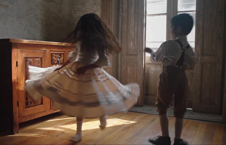 A little girl in a dress is spinning with a little boy and she falls when she stops spinning
