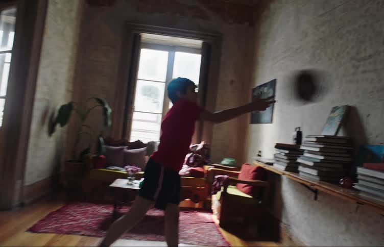 Boy throws soccer ball repeatedly against the wall in the living room