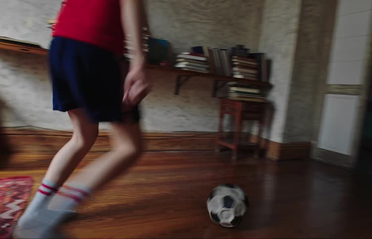 A child is kicking a soccer ball around the house