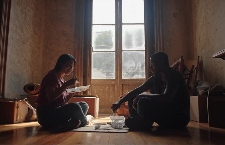 A couple eat while sitting on the floor of their apartment
