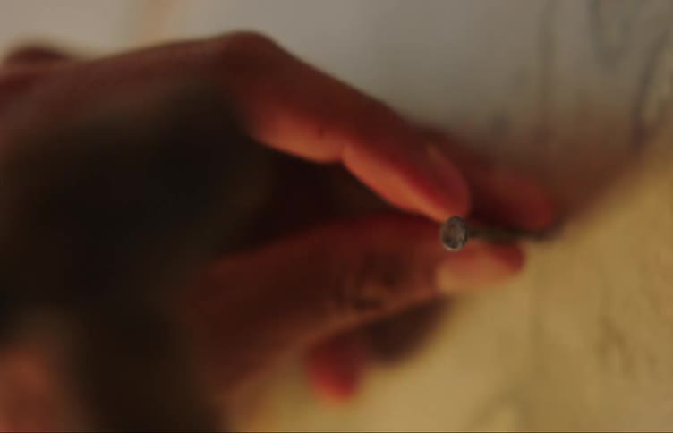 A hand holds a nail in place against a wall then hammers it in