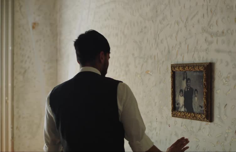 A man smiles as he hangs a framed family photograph on the wall