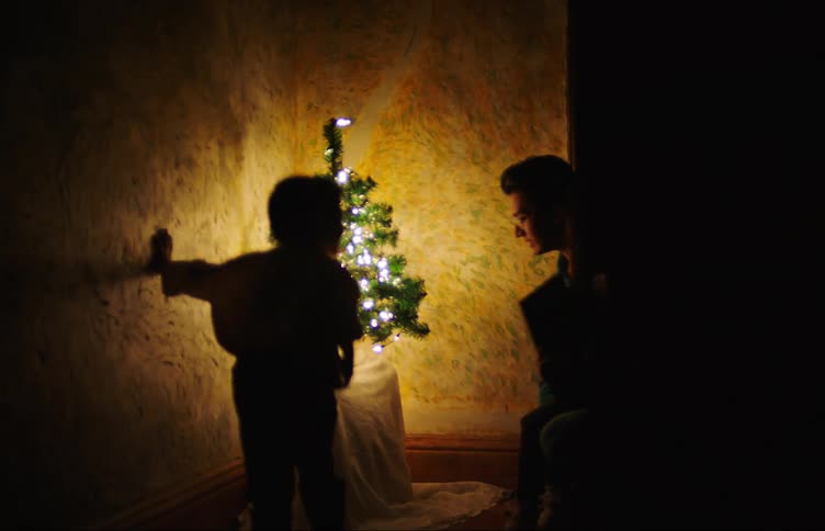 Father with his two children next to a christmas tree talking smiling smiling