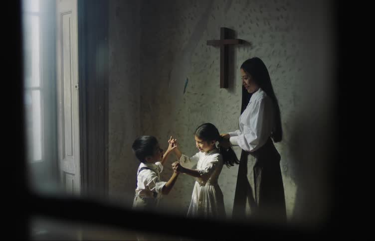 Mother fixing her daughters hair who is playing with her little brother