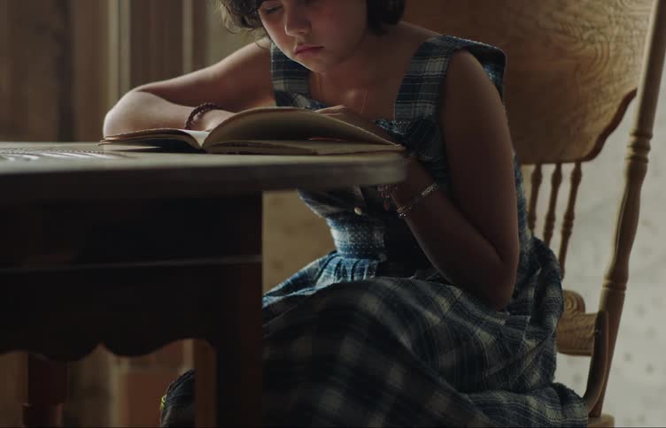 Young little girl sitting on a wooden chair reading a book