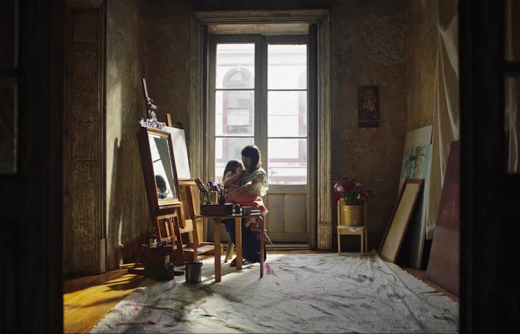 A clip of a mother sitting and lapping her child beside a window in the room