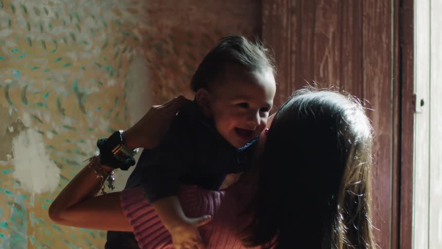 Mother holding her baby on her lap and playing with him by throwing him up while smiling a lot