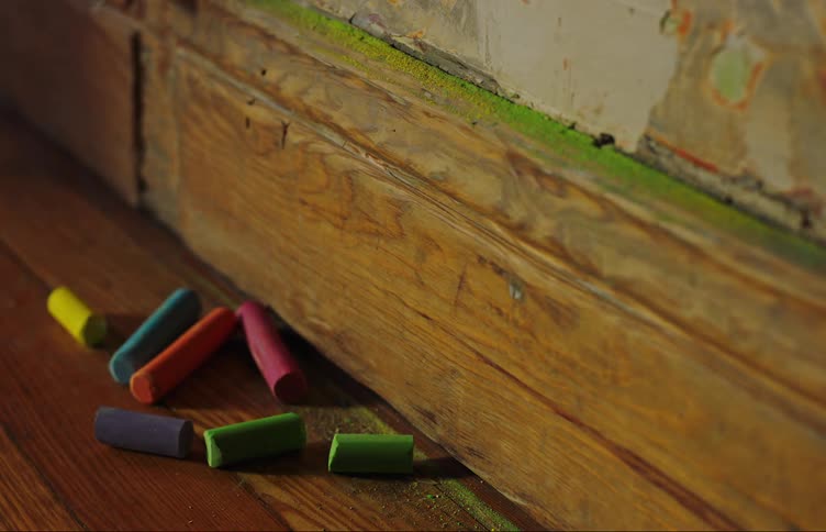 Several pieces of colorful chalk are located on a hardwood floor next to the wall