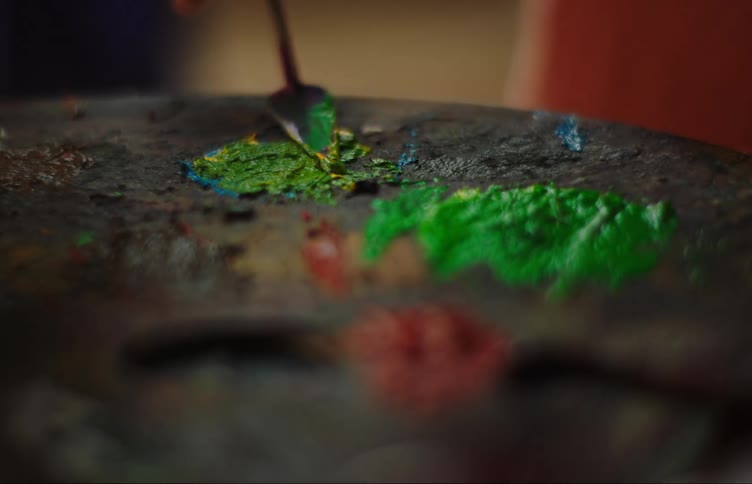 Closeup of a small spatula mixing blue yellow and green paint