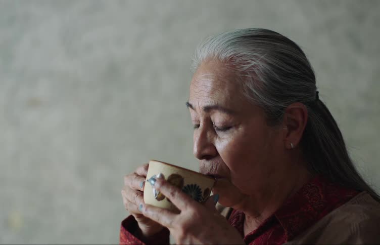 Side portrait of an elderly lady drinking a cup while indoors