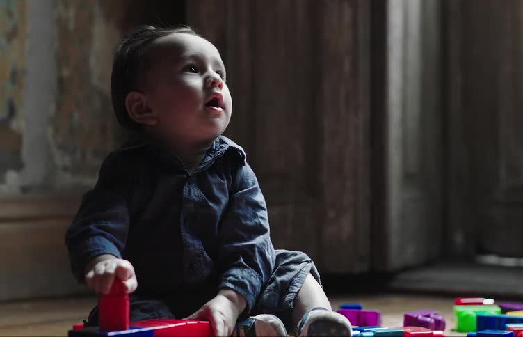 A baby sitting on the floor plays with building blocks and laughs