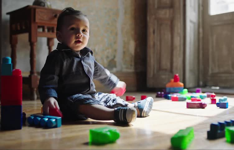 Baby sitting on a laminate floor playing with some plastic toys