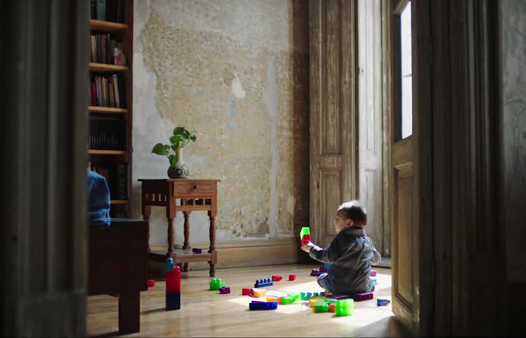 A small child plays with blocks while sitting under a window at midday