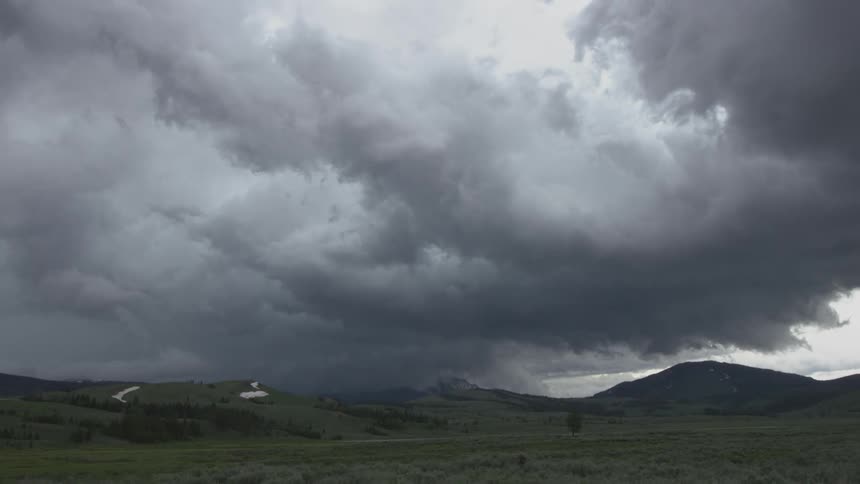 A storm moves over a plain with mountains in the background