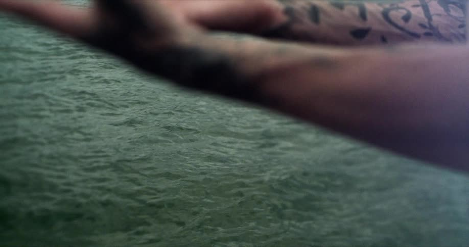 Closeup of the hands of a tattooed person stretching their arms in front of the sea in slow motion