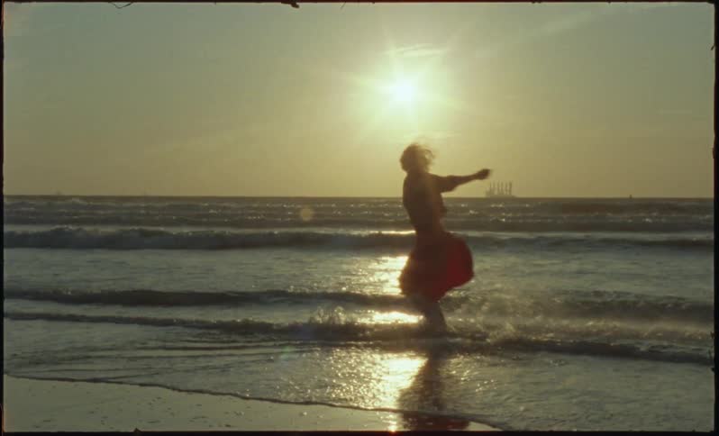 Woman running kicking and throwing sea water up with a reflection and the sun on the horizon