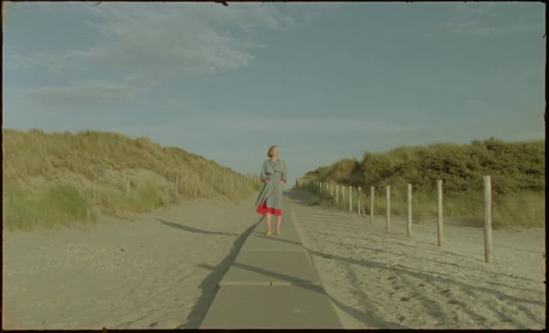 Blonde woman and a concrete dock by the sand in natural environment walking