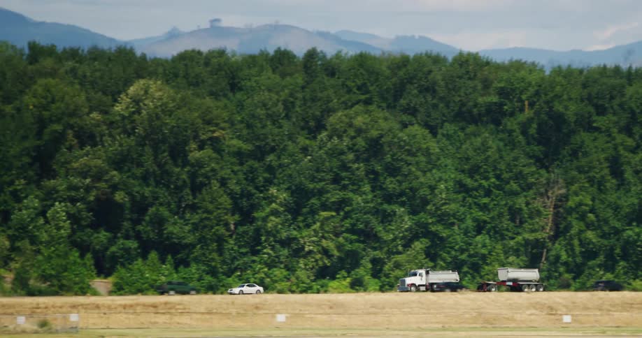 Panorama of vehicle traffic including cars and trucks on a highway at the edge of vegetation