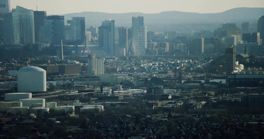 Aerial panorama of a metropolis with a skyscraper divided by a water canal with factories and silhouette of mountains on the horizon