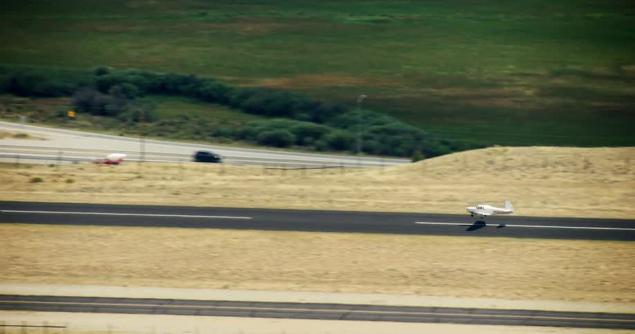 A small white airplane landing on a long narrow asphalt runway