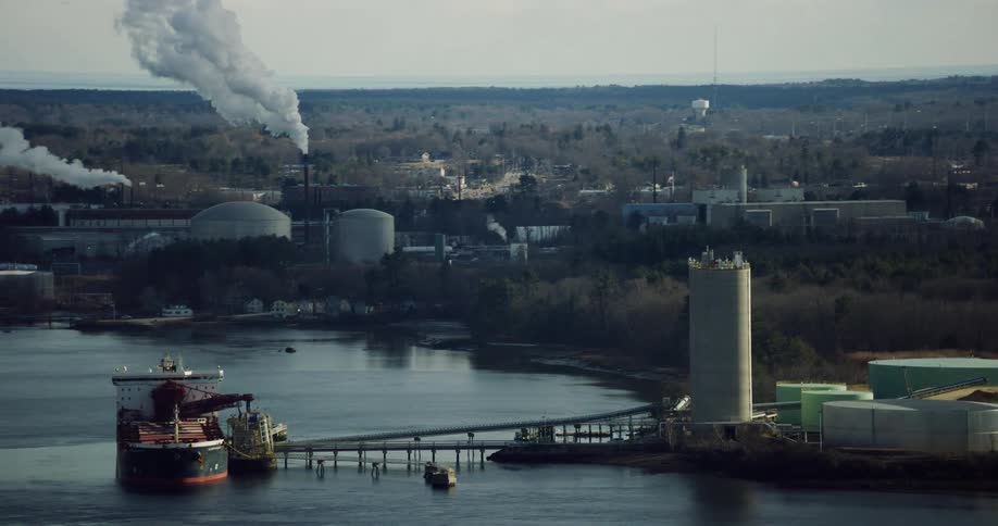 A refinery on a river belches clouds of pollution