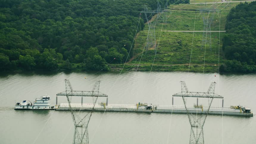 Aerial view of a large and extensive work and distribution boat passing through a river channel with power transmission lines