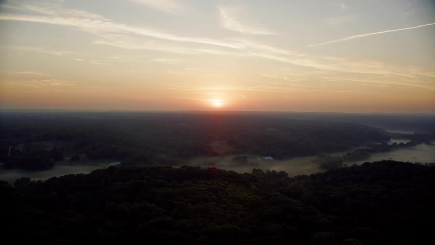Aerial landscape of hills covered in forests with a river in the middle and sunrise on the horizon
