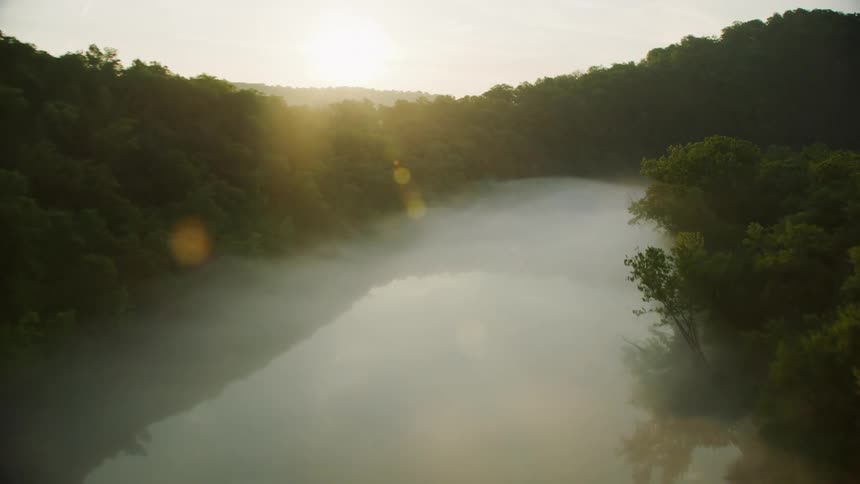 An aerial view of a foggy river surrounded by trees