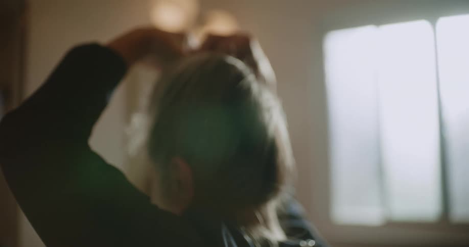 Woman tying up her hair and looking at herself in the bathroom mirror