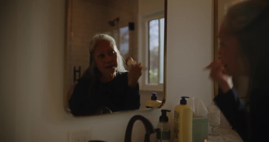 A woman puts on makeup in the mirror