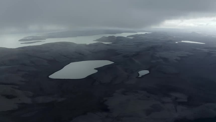 An aerial view of a region with black earth and small lakes and with a strong fog