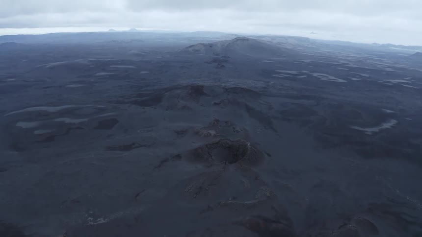 Aerial panorama of a black desert land with hills on a cloudy day
