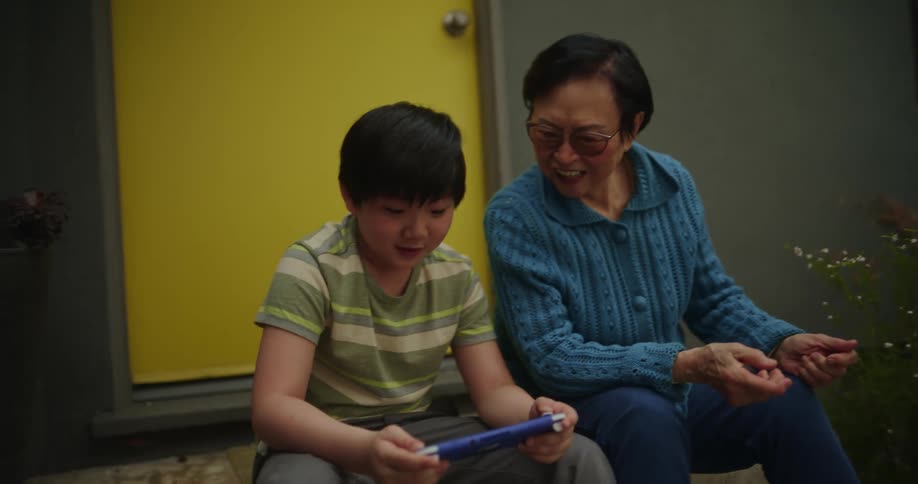 Grandmother next to his grandson and they both clap hands while playing together on a portable game
